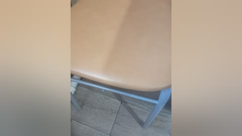 Video of a light-colored wooden chair with a smooth texture, positioned on a gray tiled floor, with a blue metal frame visible. The image has a slightly blurred, out-of-focus appearance.