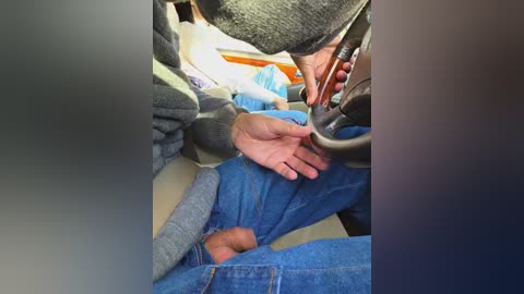 Video of a person in blue jeans and a gray sweater being restrained by two individuals in the backseat of a car. The person's hands are pinned against the seat, and the restraint appears to be a belt.