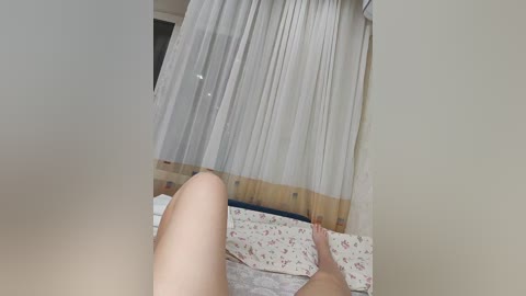 A video of a nude woman lying on a bed, viewed from below, with sheer curtains in the background.