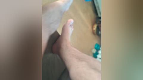A blurred video showing a pair of pale feet on a wooden floor, with a blurry background hinting at a cozy room with a TV and a blue chair.