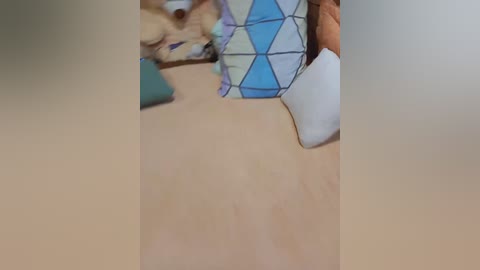 Video of a beige couch with a beige cushion and a colorful quilt featuring blue and white geometric patterns.