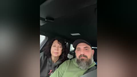A video shows a man and a woman with closed eyes, sitting in a car. The man, with a beard, wears a green shirt and a black cap. The woman, with dark hair, wears a dark jacket.