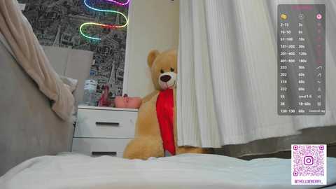 Video of a plush teddy bear in a bed, with a colorful neon light wall and a white curtain.