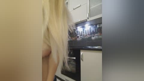 Video of a blonde woman, partially nude, leaning over a modern kitchen counter with a cityscape mural background.