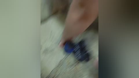 A close-up video of a person's hand holding a blue object, possibly a pen, with blurred background suggesting motion. The skin tone is light, and the hand appears to be in mid-action.