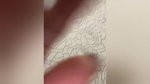 A close-up video shows a hand with visible veins and a ring on the middle finger. The background features a textured, light beige wall with a floral pattern. The image is slightly blurred.