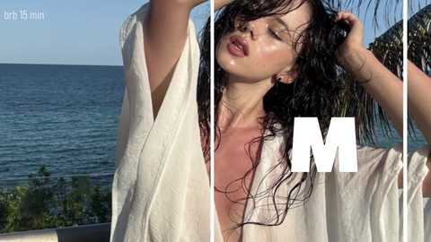 Video of a wet, sun-kissed woman with long, dark hair, wearing a white towel, standing by a sea, with \"M\" in the background.