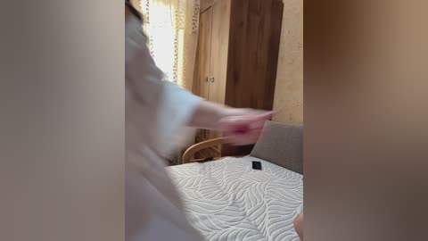 A blurry video of a person in a white shirt, likely a man, throwing a punch at a wooden door in a dimly lit room with beige walls and a bed with a white quilt.