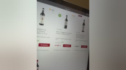 Video of a computer screen displaying an online wine store interface. The screen shows four wine bottles, each with different prices, from $4.99 to $8.99. The background is a plain white wall.