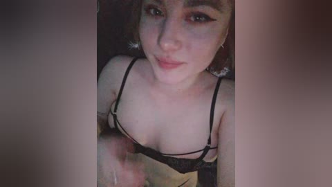 A selfie of a young woman with fair skin, brown hair, and black lingerie, taken from a high angle, showing her cleavage and breasts, with blurred background.
