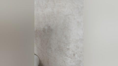 A close-up video of a pale, human forearm with a small, dark mole in the center. The background is a plain, light-colored wall. The texture of the skin appears smooth and slightly wrinkled.