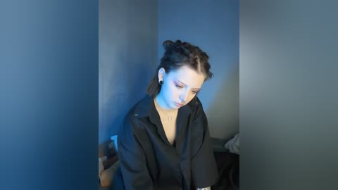 A video of a woman with dark hair in a bun, wearing a black robe, standing in a dimly lit room with blue lighting.