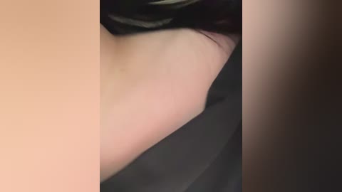 A close-up video of a person's bare back, featuring light skin and dark hair, lying on a dark surface. The focus is on the skin texture and the edge of the person's hair.