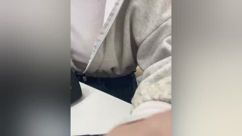 Video of a person's torso, wearing a light grey sweater and dark jeans, taken from a low angle, showing a slight bulge in the sweater.