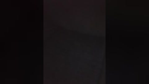 A video of a tall, dark vertical structure, possibly a building or wall, set against a completely black background, making it difficult to discern details.