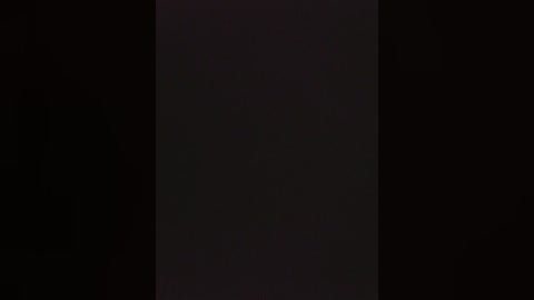 A dimly lit, black and white video of a vertical, rectangular object, possibly a piece of artwork or a textured wall, with minimal contrast and details, emphasizing shadows and minimalism.