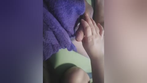 A close-up video showing a person's hand holding a purple towel over their groin area, with a blurry, indistinct background.