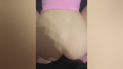 A video of a person's bare buttocks, captured from behind, showcasing fair skin and a pink garment partially covering the lower back. The setting appears to be indoors with a dark background.