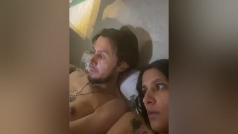A video shows a shirtless man and a woman with medium skin tones, lying on a bed, partially obscured by a blurred, beige wall.