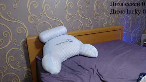 Video of a bedroom with a wooden headboard, a white decorative pillow shaped like a bear, and a lavender bedspread. Background features a patterned wallpaper with swirling designs in beige and gold. Text in Russian reads \"\u0423\u0442\u043a\u0430 \u0441\u044d\u043a\u0440\u0438\u0442!\