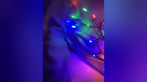 A blurred video of colorful Christmas lights against a dark background, creating a vibrant, abstract, and slightly out-of-focus composition with hues of blue, green, and red.