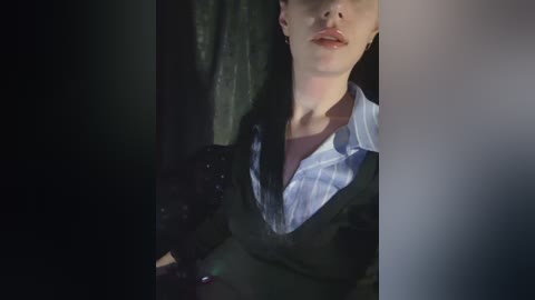 Video of a man with light skin, short blond hair, wearing a blue and white striped shirt and a dark jacket, leaning against a black curtain, dim lighting.