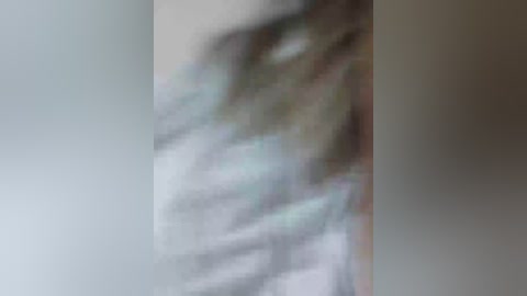 Blurry video of a person with long, wavy hair, possibly female, standing against a neutral background. The image is out of focus, making it difficult to discern specific details about the individual.