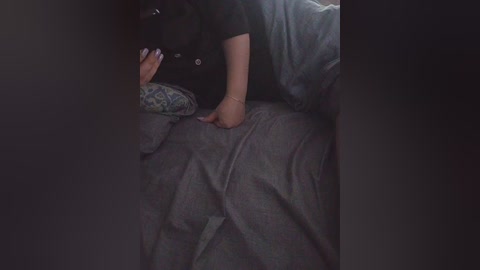 A video showing a person in a dark, cramped space, with a black hat and a gray shirt, lying on a gray bedspread, partially obscured by shadows.