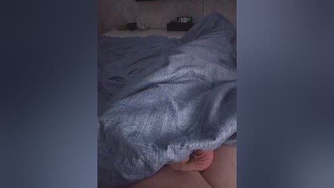 Video of a person, likely male, lying on a bed with a blue blanket, partially covered, with visible penis, in a dimly lit room with a digital clock showing 3:30.