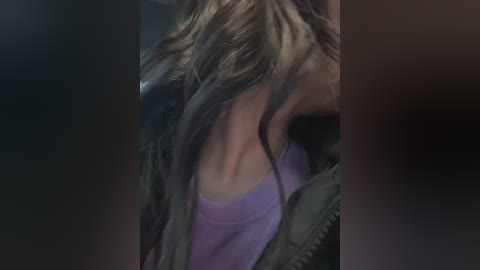 Video of a woman with long, wavy brown hair wearing a lavender tank top, partially obscured by shadows, creating a mysterious, intimate atmosphere.