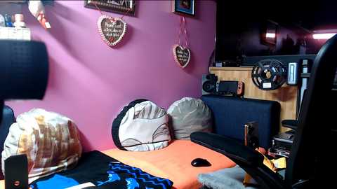 A video of a cozy RV interior featuring a purple wall with heart-shaped decorations, a black leather couch, and a cluttered wooden desk area.