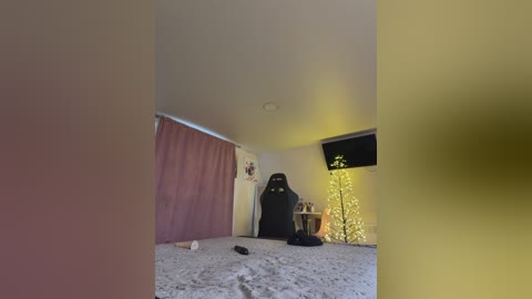 Video of a dimly lit, cluttered room with a carpeted floor, a large black gaming chair, and a lit-up Christmas tree in the corner.