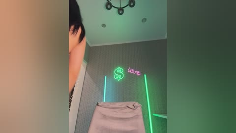 Video of a person's arm reaching into a room with green neon lights and a \"love\" sign on the wall. The room has beige wallpaper and a white ceiling with recessed lights.