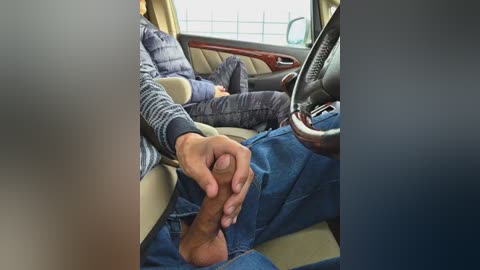 Video of a person in a car, wearing a blue puffer jacket, holding a steering wheel with a brown, curved object.