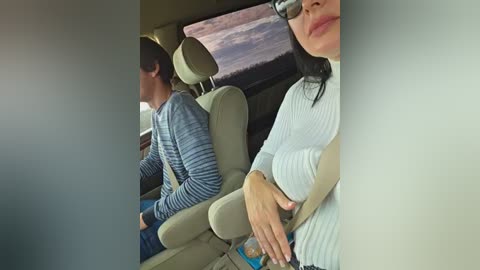 Video of a woman with glasses and a white sweater, seated next to a man in a striped shirt in a beige car, looking out the window at a desert landscape.