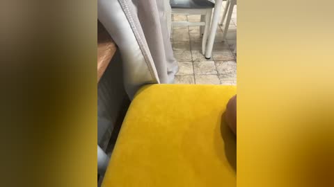 A video showing a close-up of a yellow plastic chair leg and a beige curtain, set against a tiled floor in a bright room.