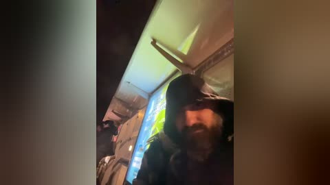 A blurry video of a man in a dark hoodie, likely taken indoors at night, with a neon green light in the background and a dimly lit room visible.