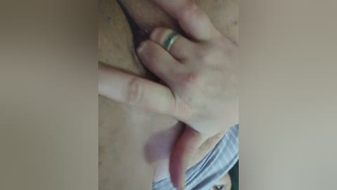 A video showing a close-up of a hand with a wedding ring, pulling down light gray fabric to expose a bare chest with light brown pubic hair.