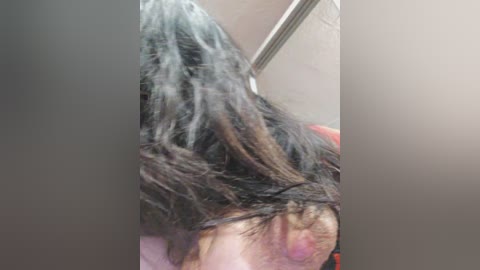 A video shows an older person with long, wet, black hair and a bruised, discolored face, possibly from a fall. The background features a beige wall and a metal door handle.