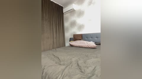 Video of a modern bedroom with a gray bedspread, a gray headboard, a pink pillow, and beige curtains. Air conditioner is mounted on the white wall.