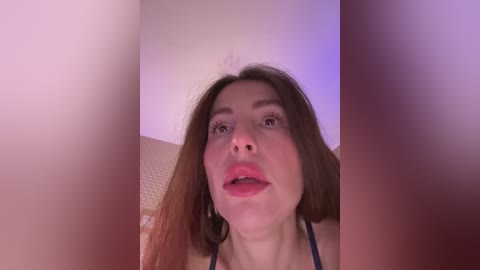 A close-up video of a young woman with long brown hair, light skin, and full lips. She's wearing a black top, and the background is blurred.