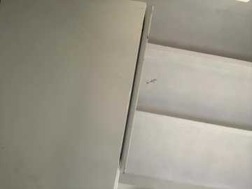 Video of a minimalist interior wall featuring a large, smooth, white panel with a thin, vertical crack running down its center. The background reveals a light gray ceiling with horizontal lines, indicating a textured surface.