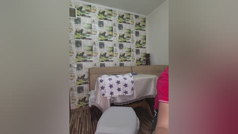 A video of a small, neatly arranged bedroom with a bed covered in a star-patterned quilt, a beige carpet, and wallpaper featuring newsprint and cityscapes.