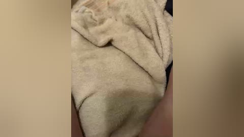 Video of a person's lower torso wrapped in a beige towel, showing folds and texture. The background is blurred with a soft beige color, focusing attention on the towel.