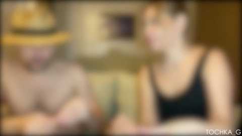 Blurry video of two people, a man in a hat and a woman in a black tank top, possibly discussing something in a dimly-lit room.