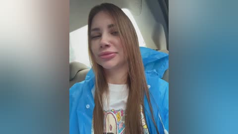 Video of a young woman with straight, light brown hair, wearing a blue raincoat over a white T-shirt with a colorful graphic design, sitting in a car seat, with a neutral expression.