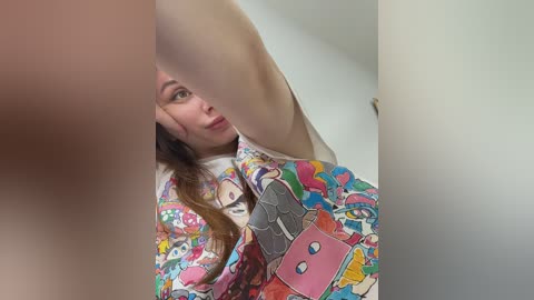 Video of a young woman with long brown hair, wearing a colorful, patterned shirt featuring cartoon characters, seen through a white, textured surface.