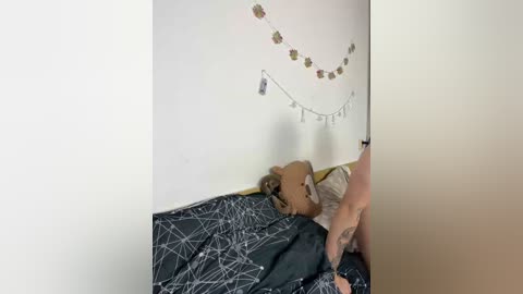 A video shows a small child with fair skin and light brown hair, lying on a bed with a dark blue and white geometric patterned duvet. A hand reaches out to the child.