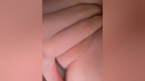 A close-up video of a pair of light-skinned hands, fingers gently touching each other, set against a soft pink background. The image is slightly blurry, with a soft, diffused lighting that creates a gentle, intimate atmosphere.