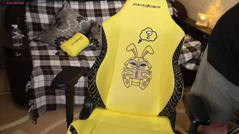 Video of a yellow gaming chair with a cartoon car design, placed in a cozy living room with a plaid blanket, cushions, and a lit candle.